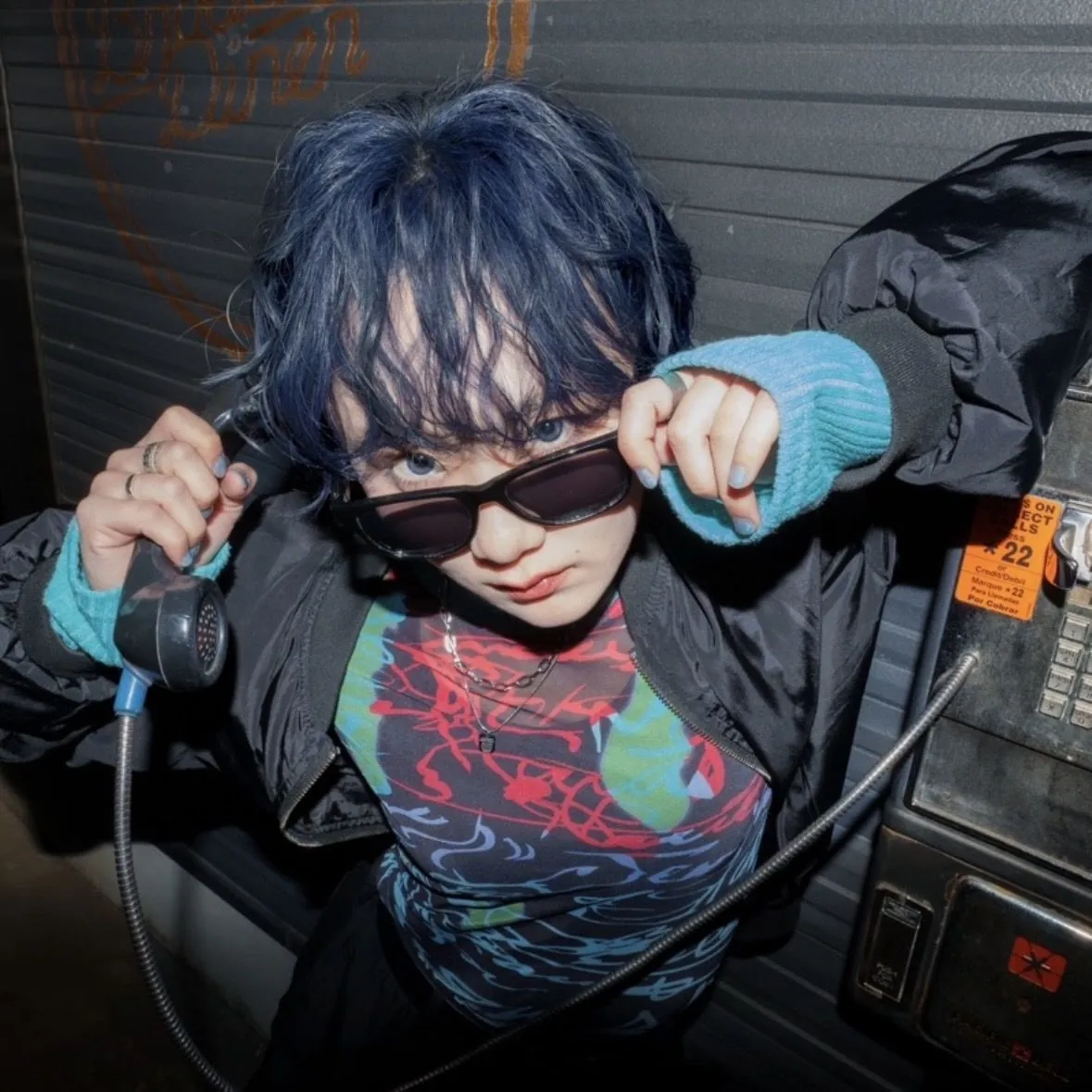 公衆電話の前でサングラスをずらすMetalina